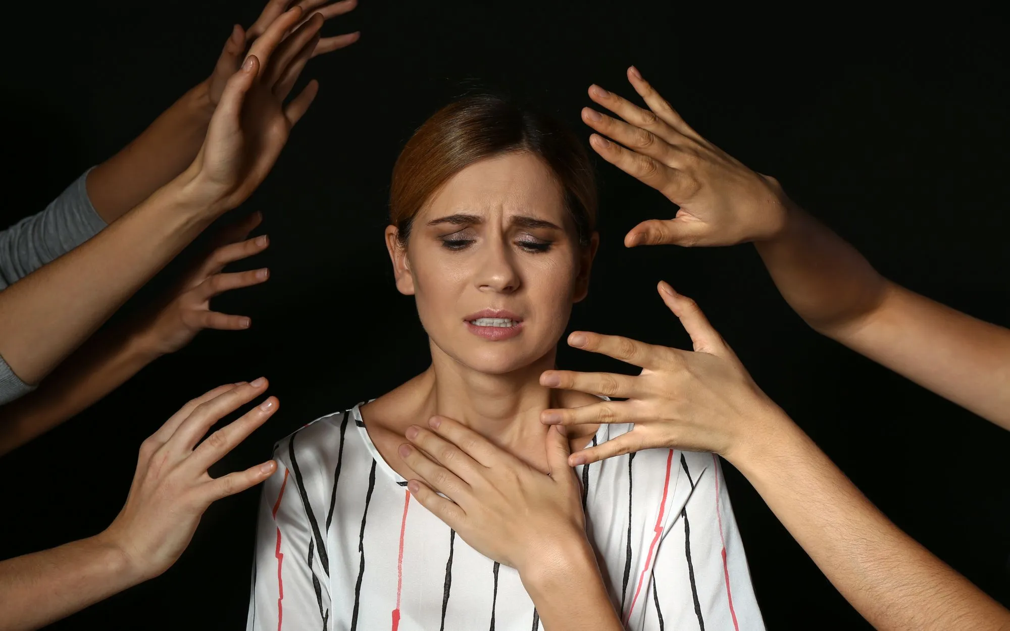 Mujer con gesto de agobio rodeada de manos que se extienden hacia ella sobre un fondo oscuro, como representación de la ansiedad